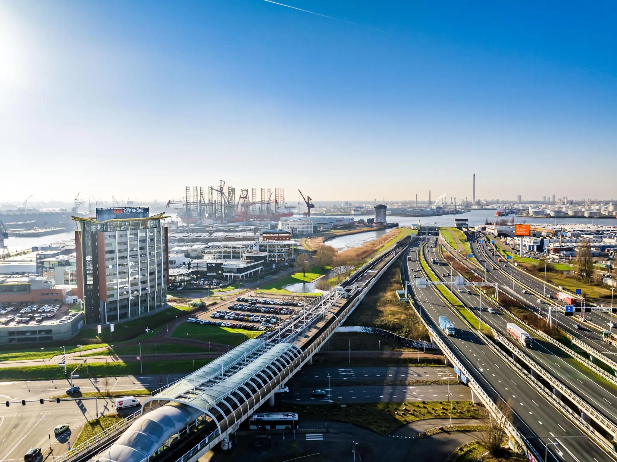 Luchtfoto van de Karel Doormanweg in Rotterdam met snelweg, treinspoor en havengebied op de achtergrond.